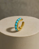 Gold ear cuff with turquoise stones on a beige plate