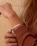 Close-up of a person wearing a gold bracelet on a beige background
