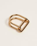 A polished gold metal ring with a unique double-looped design, shown on a clean, light off-white background.