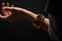 Hand wearing multiple beaded bracelets on a dark background