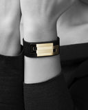 Black leather bracelet with gold accents on a wrist against a neutral background