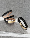 Black leather bracelets with gold clasps on a textured surface