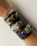 Black natural horn cuff bracelets with colorful gemstones on a wrist against a white background