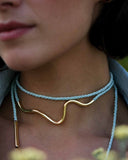 Close-up of a woman wearing a gold necklace with a blue cord