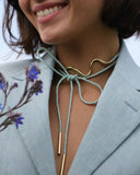 Woman wearing a gold necklace with a light blue cord, smiling.