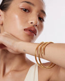 Close-up of a person wearing a gold bangle bracelet on a plain background