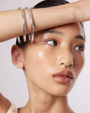 Close-up of a person wearing a large silver bangle bracelet with a neutral background