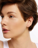 Close-up of a person wearing a small stud earring on a plain background