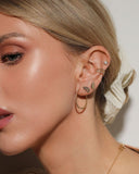 Close-up of a person wearing gold earrings and ear cuffs with a neutral background