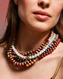 Close-up of a woman wearing a colorful layered beaded necklaces against a pink background