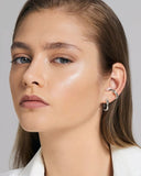 Close-up of a woman wearing a silver ear cuff and earring against a neutral background