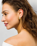 Close-up of a woman wearing gold hoop earrings with a neutral background