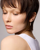 Close-up of a woman with a short haircut and drop earring against a neutral background