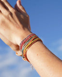 Close-up of a wrist with colorful silk bracelets against a blue sky.