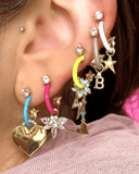 Close-up of an ear with multiple colorful earrings and charms including hearts, stars, and letters.
