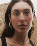 Woman wearing gold hoop earrings and a necklace, with a straw hat in the background
