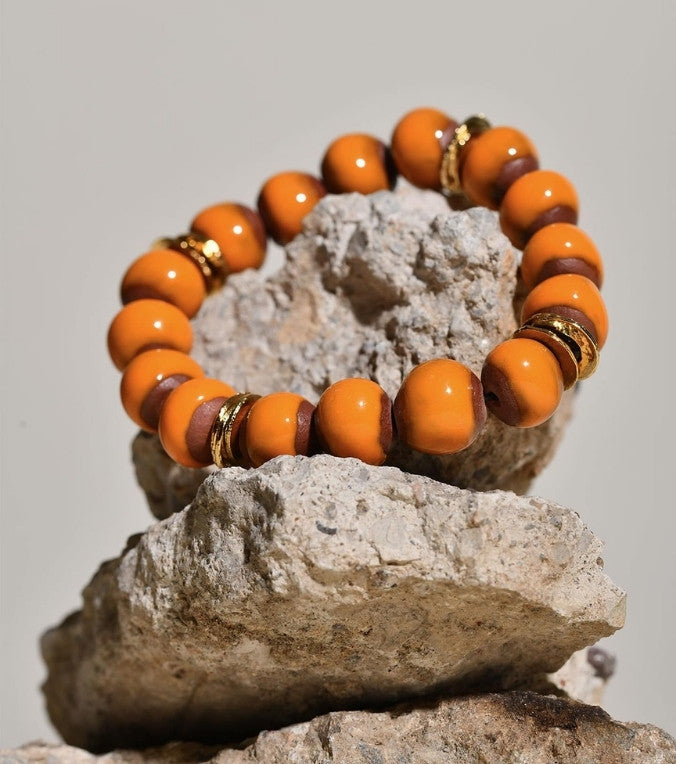 Orange beaded bracelet with gold accents on a rock