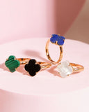 Four rings with colorful stone designs on a pink background