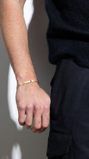 Man wearing a gold bracelet on a neutral background