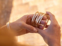 Hands holding a collection of gold bracelets against a warm, blurred background