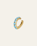 Gold hoop ear cuff with blue gemstones on a beige background
