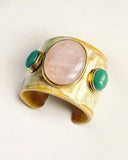 Gold natural horn cuff bracelet with pink stone and green stones on a white background