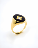 Gold pinky ring in black enamel with center stone on a white background