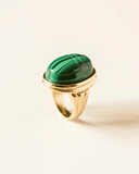 Gold ring with a green gemstone on a beige background