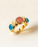 Gold ring with pink and blue gemstones on a beige background
