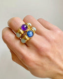Gold rings with purple and blue gemstones on a hand against a plain background