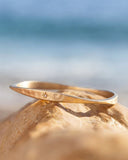 Gold bracelet on a rock with a blurred beach background