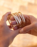 Hand holding multiple gold bracelets with a warm, blurred background