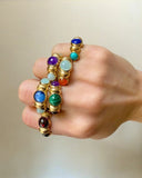 Hand wearing a colorful gemstone rings on a neutral background