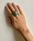 Hand wearing a green ring on a plain background