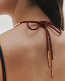 Close-up of a person wearing a burgundy necklace with a gold bar accessory.