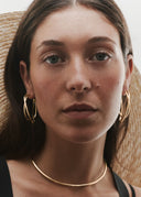 Woman wearing gold hoop earrings and a gold necklace with a neutral background
