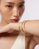 Mini gold bangle bracelet on a wrist with a neutral background