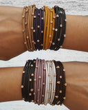 Multiple leather bracelets with stones on a person's wrist against a light background.