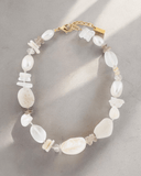Necklace with white stones, pearls, and gold clasp on a light gray background