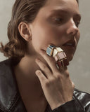 Woman wearing large, colorful ring on her finger against a neutral background