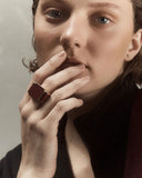 Person wearing a ring with a dark stone on a neutral background