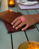 Hand wearing a pink ring on a wooden surface with a blurred background