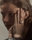 Close-up of a person with a hand covering part of their face, wearing a ring.