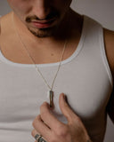 Man wearing a white tank top and holding a necklace with a pendant.