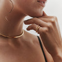 Close-up of a person wearing a gold necklace and ring, with a neutral background.