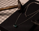 Necklace with a green gemstone pendant on a black surface with tools in the background