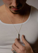 Man wearing a white tank top and holding a necklace with a pendant.