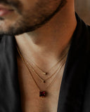 Close-up of a man wearing a gold necklace with a red gemstone pendant.