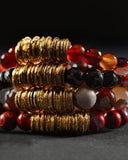 Stack of beaded bracelets with gold, red, and black beads on a dark background