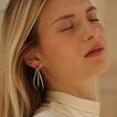 Close-up of a woman wearing gold hoop earrings with a neutral background